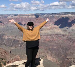 Young woman with her arms in the air standing in front of a canyon